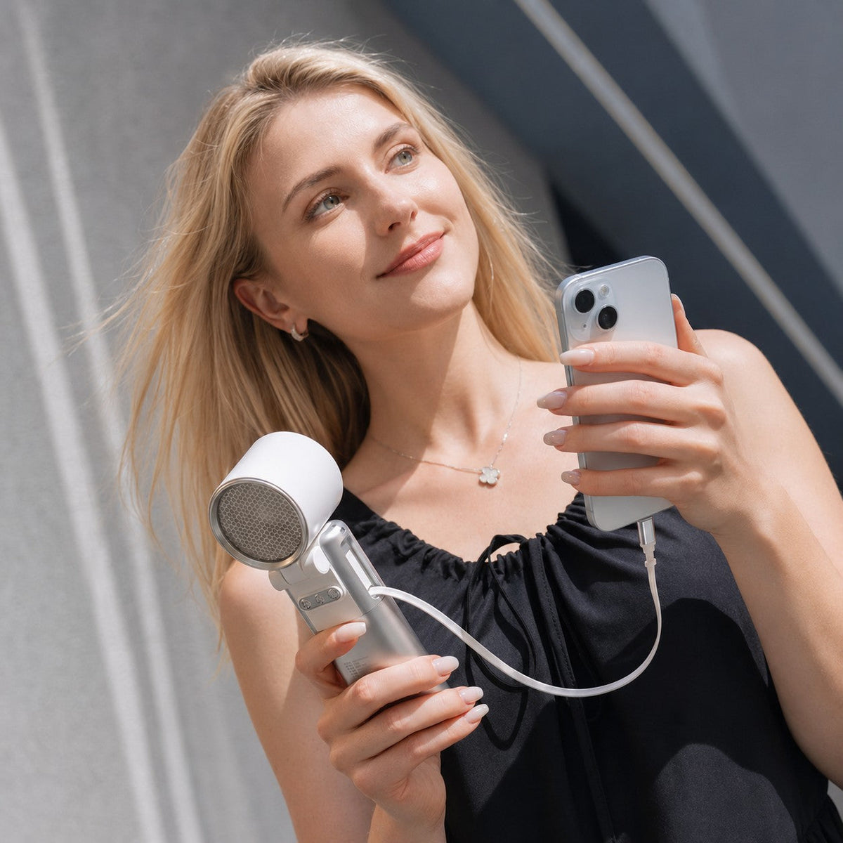 Blonde woman holding a white and silver CapyUltra portable turbo fan charging a silver smartphone outdoors.