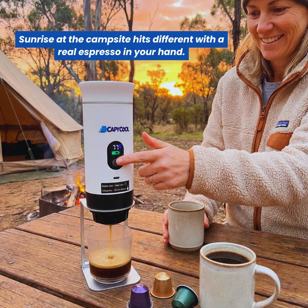Woman brewing espresso with a white CapyPress portable coffee machine at a campsite during sunrise.