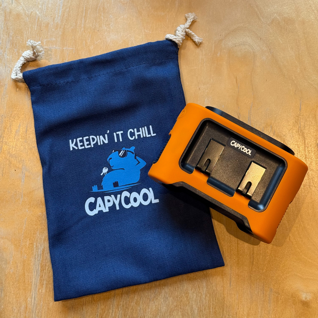 Navy blue Capycool Chill Bag drawstring pouch with a capybara logo next to an orange and black cooling device.