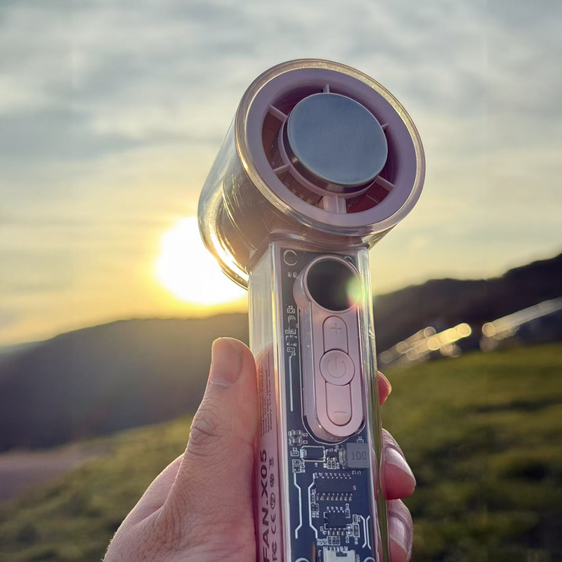 Hand holding a transparent mecha cooling fan with a pink head and ice compress, against a sunset.